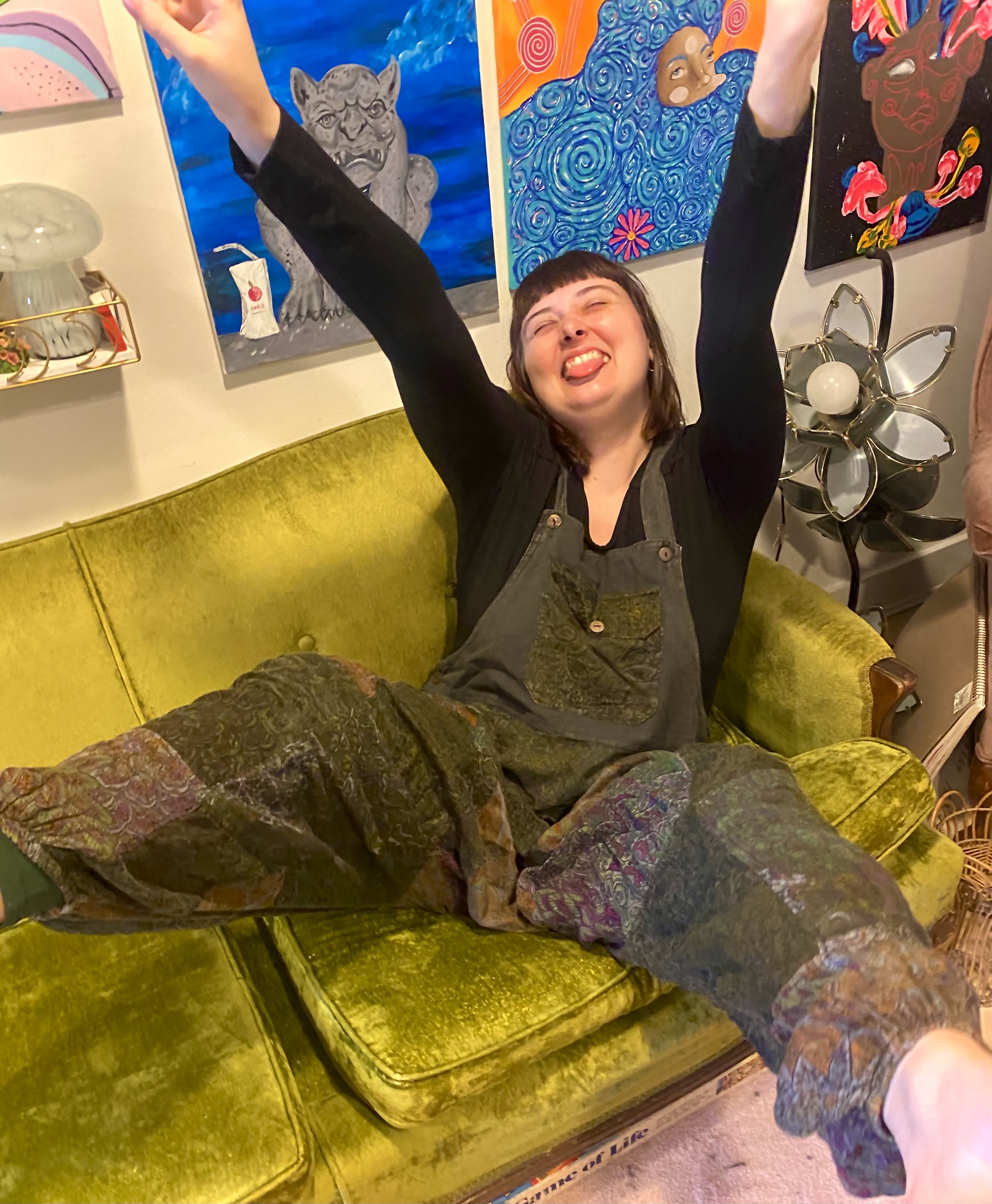 Tianna celebrating in a green chair surrounded by colorful original artwork.