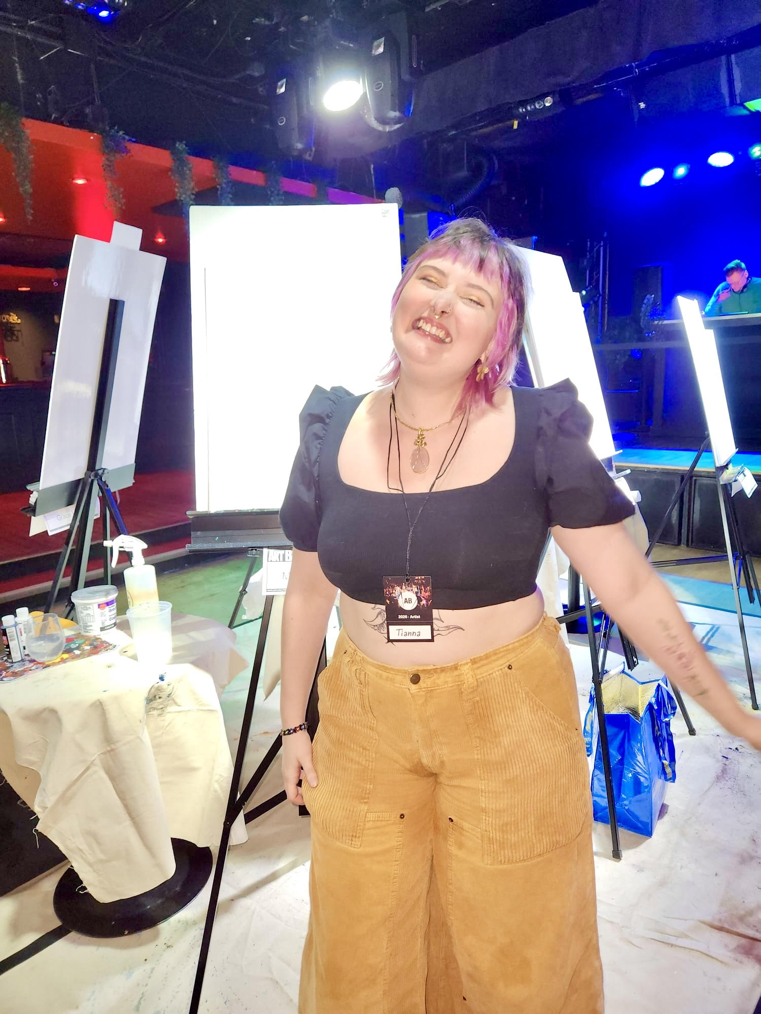 Tianna Hall smiling at an art event with canvases and studio supplies behind her