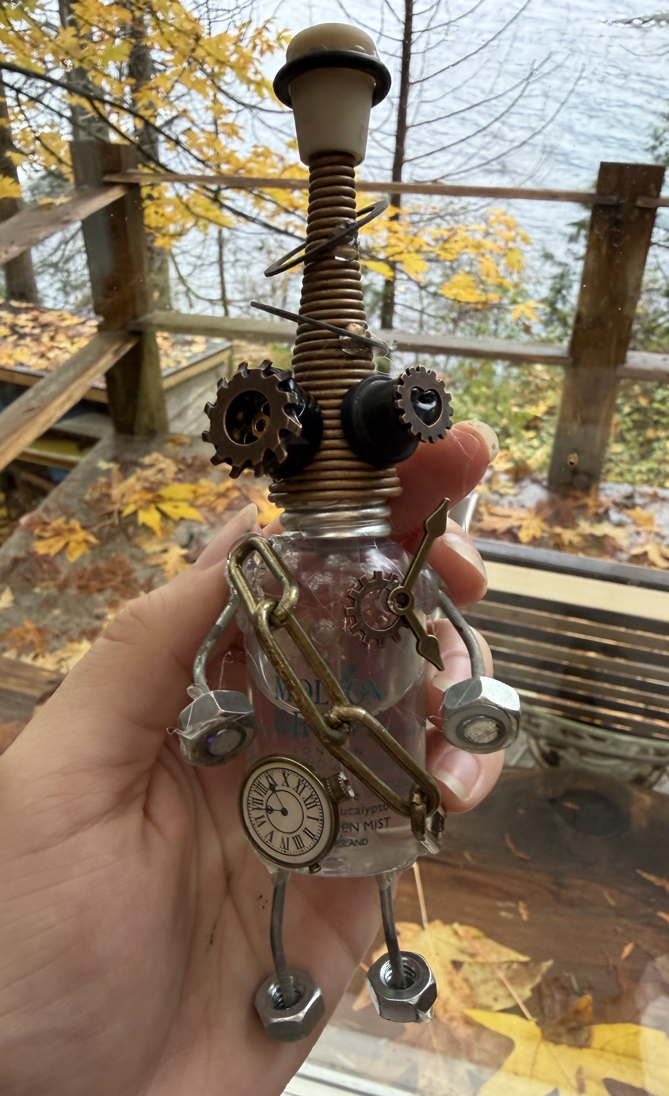 A handmade junk robot held in someone's hand with metal parts, antenna details, and a small face.